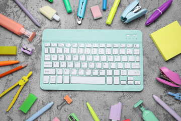Composition with computer keyboard and school supplies on grey grunge background, closeup
