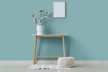 Pouf, table and vase with cotton flowers near green wall in interior of living room