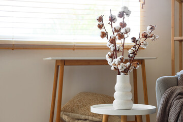 Vase with cotton flowers on table near window in interior of living room, closeup