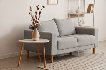 Interior of living room with comfortable sofa, table and vase with cotton flowers