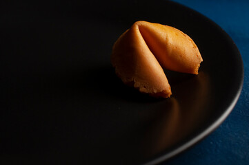 Fortune cookie on a dark plate on a blue table. copy sapce