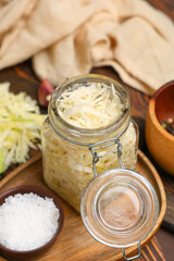 Jar with tasty sauerkraut and bowl of salt on wooden background, closeup