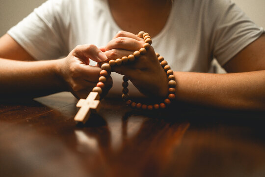 Hands holding wooden rosary beads with christian cross - Catholic prayer and faith devotion