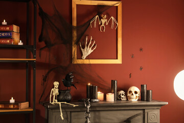 Skulls with burning candles on fireplace in room decorated for Halloween