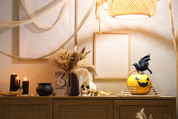 Halloween decor with burning candles on chest of drawers in room