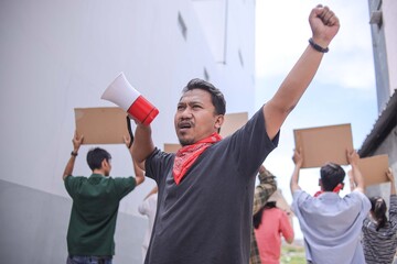 Asian Male Activist Using Megaphone To Amplify Voice And Raising Hands While Leading Group
