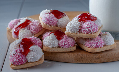 Marshmallow cookies with coconut flakes and strawberry jam on top with a glass of cold milk on the side, foods high in sugar and carbohydrates, side view close up