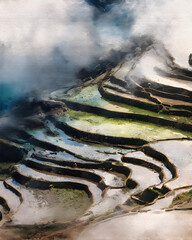 Rice terraces cascade down the mountainside in Yunnan, China, reflecting the sky and clouds in their flooded fields, creating a serene and picturesque landscape.