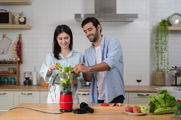 Couple making fresh vegetable smoothie together in modern kitchen with blender for healthy lifestyle concept