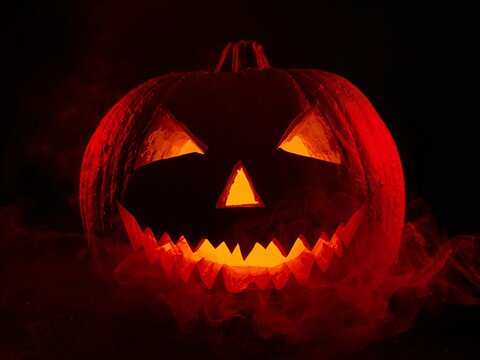 A spooky Jack-o'-lantern with a glowing face, surrounded by eerie red smoke on a black background.