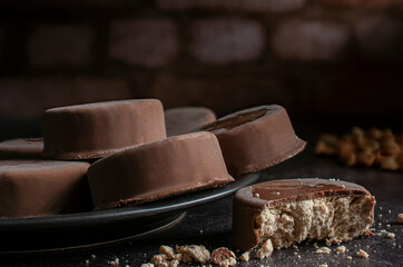 MAZAPAN, a dessert originally from Spain and Mexico made with peanuts and covered in chocolate. Mazapan on a black plate with a brick wall in the background. Foods high in sugars and carbohydrates.