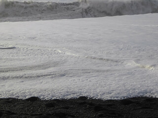 A detailed close-up captures the intricate, bubbly texture of white sea foam as it recedes from the...