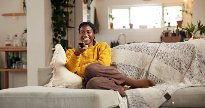 Happy, black woman and watching tv on sofa with remote for channel, movie or entertainment in home. Female person, user or smile with online subscription for series, news or show on couch in house