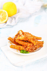 Spicy Glazed Chicken Feet with Sesame Seeds and Lemon Garnish on White Plate
