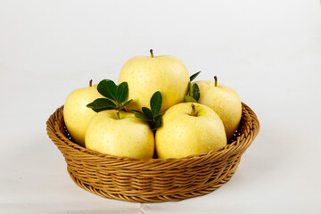 Fresh Yellow Apples in Wicker Basket with Green Leaves on White Background