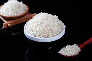 White Long Grain Rice in Bowls and Spoon on Black Background for Cooking and Food Preparation