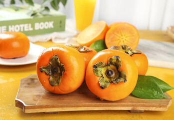 Fresh Orange Persimmons on Wooden Board with Juice Glass and Green Leaves in Modern Kitchen