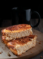Cornbread on a round cutting board with a black cup and black background, on a rustic wooden table