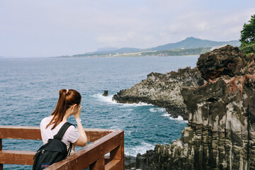 A woman is taking a photo of Jusangjeolli cliffs with basalt columns.