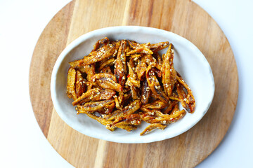 Crispy fried anchovies with sesame, dried chili, green peas, and herbs on white background.