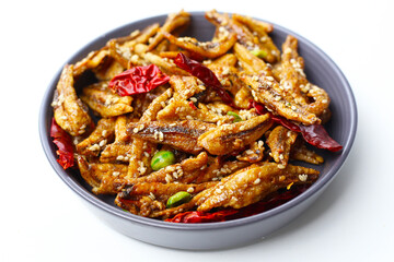 Crispy fried anchovies with sesame, dried chili, green peas, and herbs on white background.