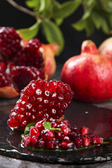 Fresh Red Pomegranate Seeds and Arils on Black Slate with Whole Fruits