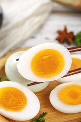 Hard-boiled eggs with golden yolks on wooden cutting board with chopsticks and herbs