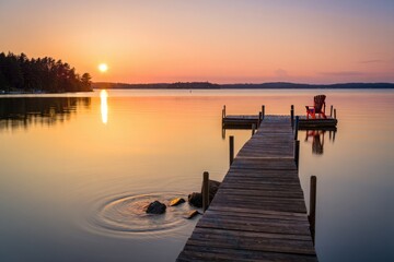 Fototapeta premium Tranquil Lake Sunrise Over Wooden Dock With Red Chair
