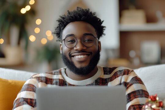 Smiling young man talking on a video call via laptop, sitting at home on the sofa, showing a New Year's gift to the camera, extending holiday greetings, Generative AI - Powered by Adobe