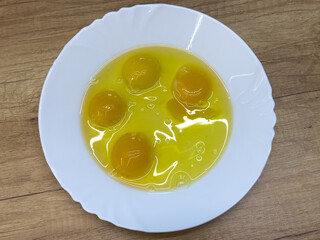 Four raw eggs with yolks and whites in a white bowl, close-up view of fresh ingredients for cooking...