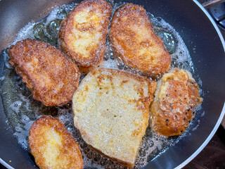 Slices of bread frying in hot oil in a pan, close-up view of golden brown toast preparation.
