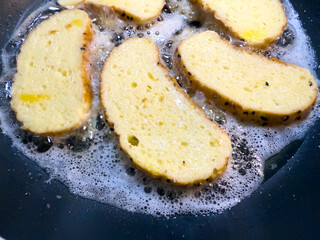 Bread slices frying in oil on pan, bubbles around edges, gas stove in kitchen.