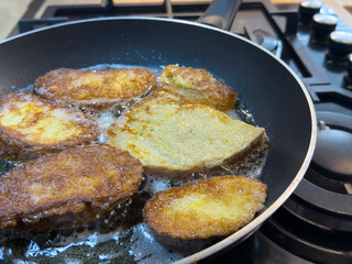 Bread slices frying in oil on pan, golden brown surface, gas stove visible in kitchen.