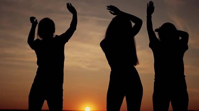 Silhouette of three woman dancing at sunset in open field with warm dusk sky and glowing sun silhouette creating celebration vibe friend gathering and joyful dance under orange sky in outdoor setting