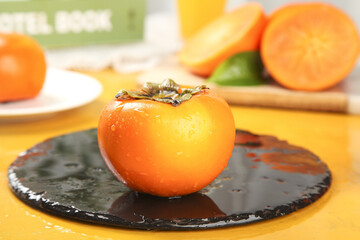 Fresh Ripe Persimmon Fruit on Dark Plate with Sliced Persimmons in Kitchen Setting