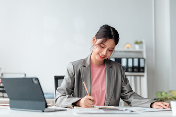 Asian businesswoman writing on notebook and working with digital tablet computer at office desk