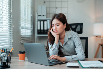 Young Asian businesswoman feeling stressed and exhausted while working on a laptop at her office desk, facing tight deadlines and pressure