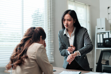 Asian businesswoman displaying time on her smartwatch to an employee in a busy office, highlighting the pressures of deadlines and projects