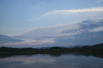 Peaceful lake landscape with blue sky, white clouds and mountains reflected in calm water at twilight