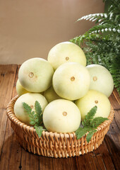 Fresh Yunnan White Melons in Wicker Basket on Wooden Table with Fern Leaves