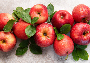 Fresh red apples with green leaves resting on gray surface