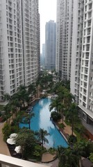 Fototapeta premium High-rise apartment complex with a tranquil pool area, showcasing lush greenery and modern architecture.