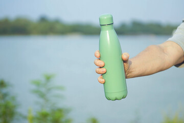Reusable hydration solution: man presenting insulated bottle against nature background. Eco friendly living and zero waste movement. Conscious consumerism, climate action, sustainable choices concept