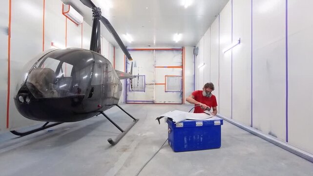 Worker In Protective Gear Sanding Metal Parts Of Helicopter Undergoing Maintenance - Robinson R44 Helicopter Inside Hangar. - wide shot