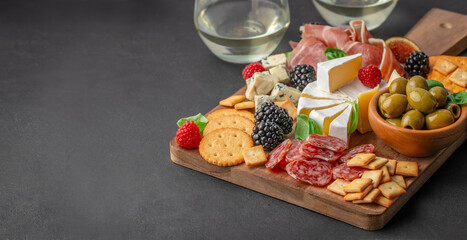 Assorted antipasto board with cheese, cured meats, olives, crackers, figs, and berries on a wooden serving board, dark background, top view