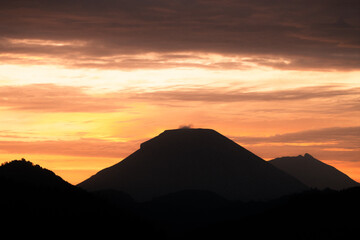 Beautiful silhouette of mountain peaks and forested hills during sunrise with dramatic orange and purple sky in the background.