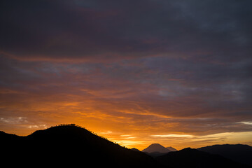 Silhouette of a mountain with dramatic glowing sunrise sky and soft clouds above, creating a peaceful nature landscape.