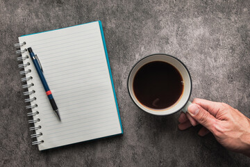 Coffee Cup in Hand with Notebook and Pen on Desk