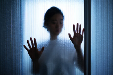 Silhouette of a person's face and hands pressed against frosted glass in dim blue light image photo