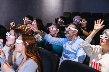 Multi ethnic group of excited people wearing 3d glasses watching a movie in the cinema, pointing and raising hands
